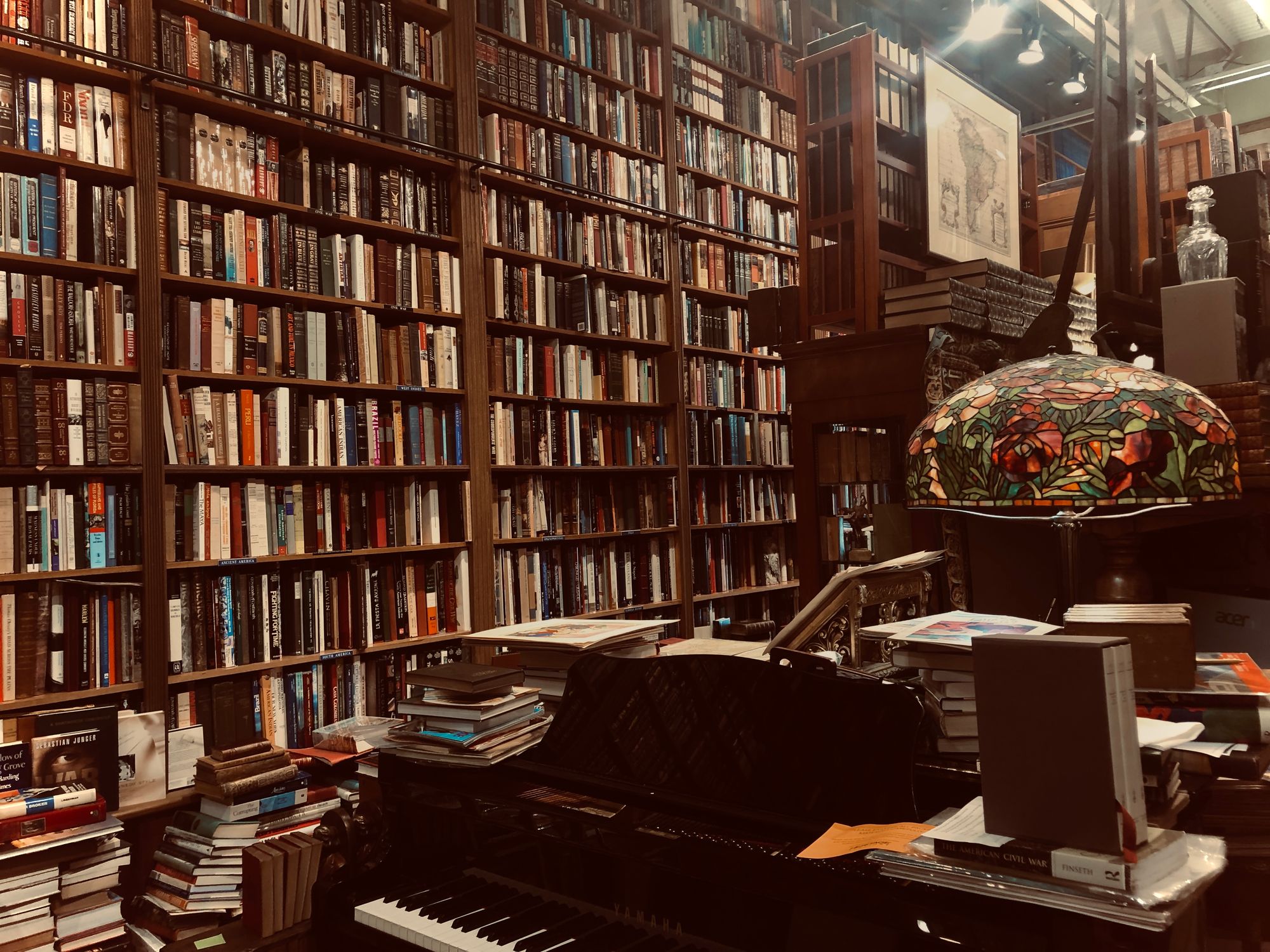 Interior of a classic bookstore with wall-to-wall wooden bookcases. Piano and antiques in the center of the room.