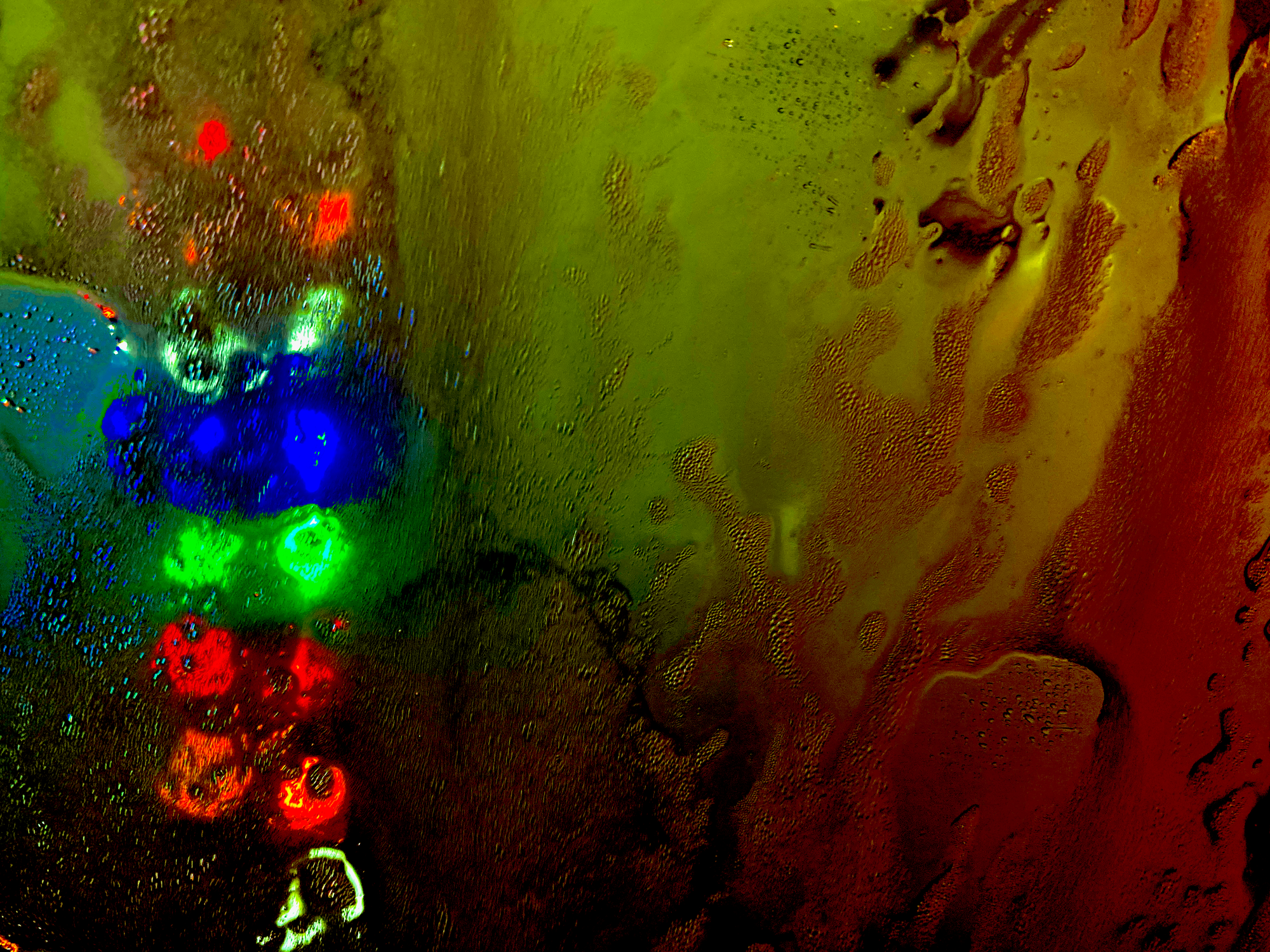 Foamy water and red-blue-green colored-stoplight as seen from a car’s windshield glass.