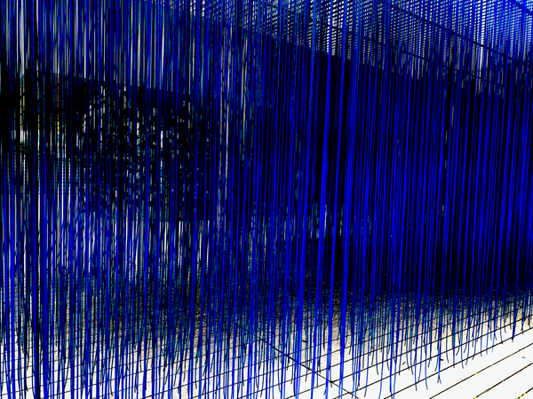 Art installation showing long blue threads hanging from the ceiling echoing the programmable logic gates in computing.